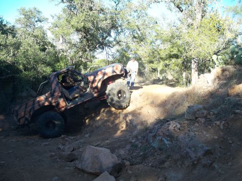 1996 Ford Bronco - A custom-painted, lifted Ford Bronco is navigating a steep, rocky off-road trail with a person standing nearby. The vehicle has large tires…