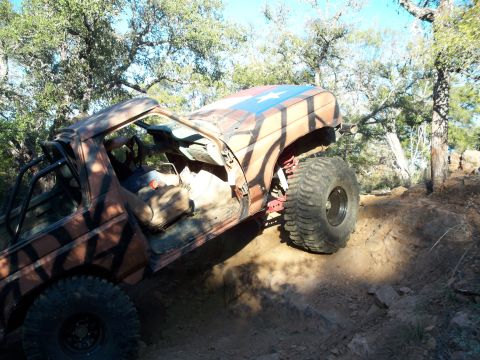 1996 Ford Bronco - A heavily modified Ford Bronco with large off-road tires is navigating a steep, rocky incline. The vehicle has a camouflage paint scheme an…