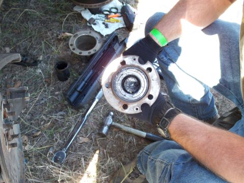 1996 Ford Bronco - A person works on a vehicle's wheel hub assembly with tools laid out on the grass.