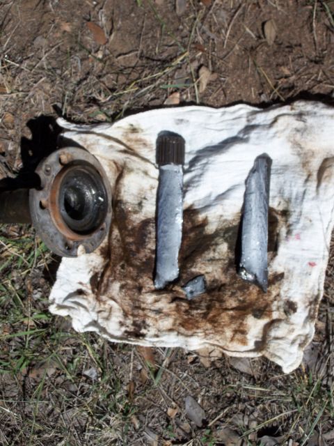 1996 Ford Bronco - Broken axle shaft and hub assembly parts laid out on a stained cloth on the ground.