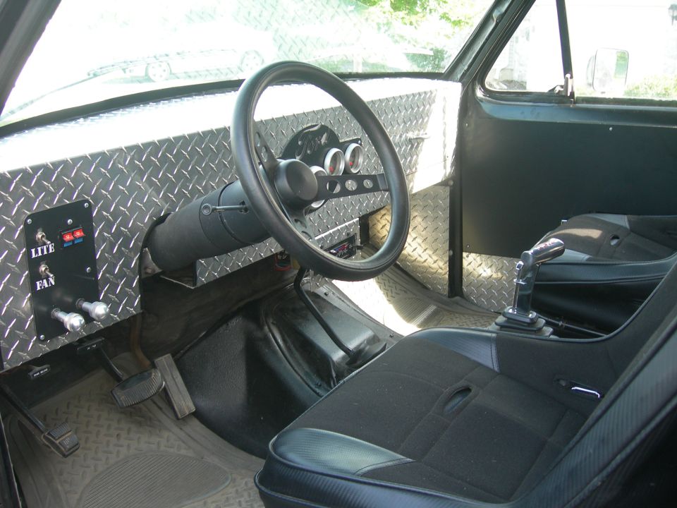 Custom interior with diamond plate dash, aftermarket steering wheel, and racing seat. Toggle switches labeled LITE and FAN