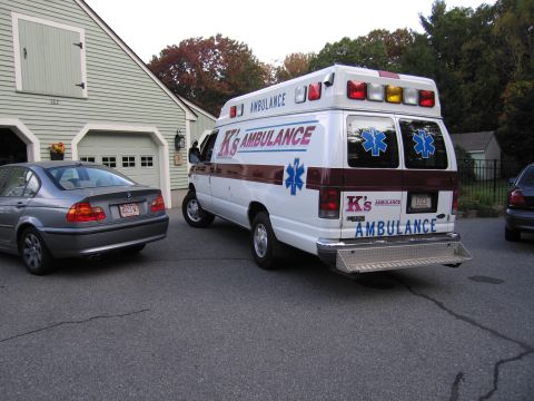 2001 Ford Crown Victoria - An ambulance van and a sedan are parked in a driveway next to a garage.