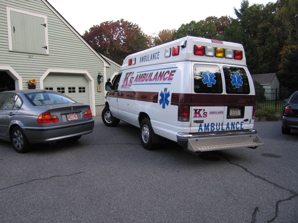 Ambulance van with K's AMBULANCE text parked next to a gray sedan
