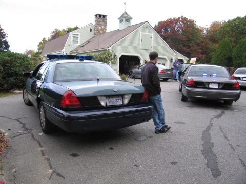 2001 Ford Crown Victoria - Two police cruisers are parked in front of a light green building with a cupola.