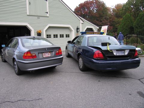 2001 Ford Crown Victoria - Two cars, a police Crown Victoria and a BMW sedan, are parked outside a garage.