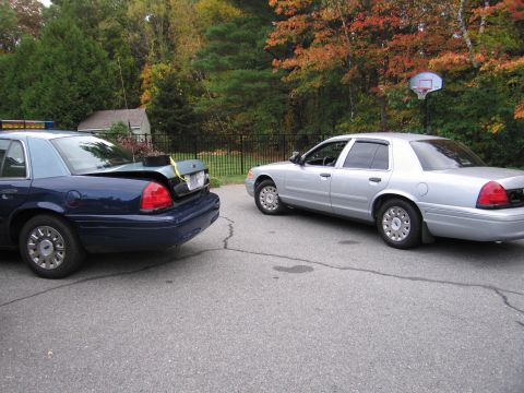 2001 Ford Crown Victoria - Two Ford Crown Victoria police cars are parked on an asphalt surface with trees in the background.