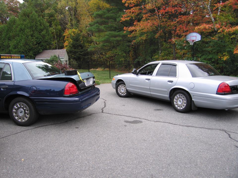 Two Ford Crown Victorias, one blue with trunk open, the other silver, parked on asphalt