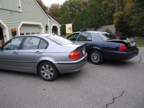 2001 Ford Crown Victoria - A dark blue police car is parked next to a silver sedan, with its trunk open.