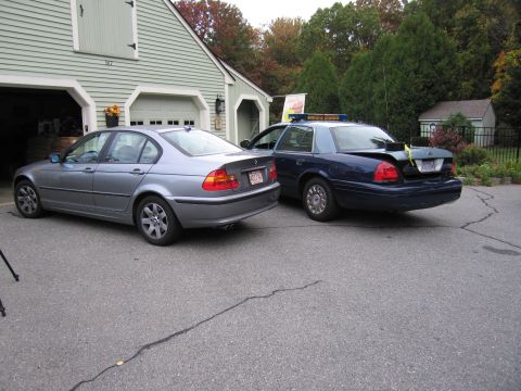 2001 Ford Crown Victoria - Two sedans, one a police car, are parked in front of a garage.