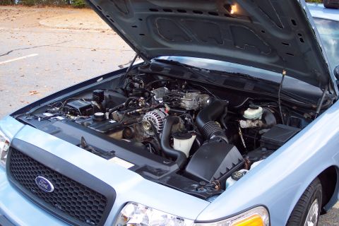 2001 Ford Crown Victoria - The engine bay of a light blue 2001 Ford Crown Victoria is visible with the hood raised.