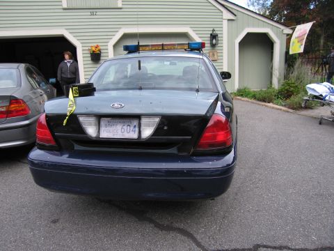 2001 Ford Crown Victoria - A dark blue police car is parked in front of a garage, with another car to its left.