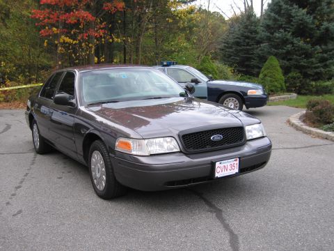 2001 Ford Crown Victoria - A dark gray 2001 Ford Crown Victoria is parked in front of a police car, with autumn foliage in the background.