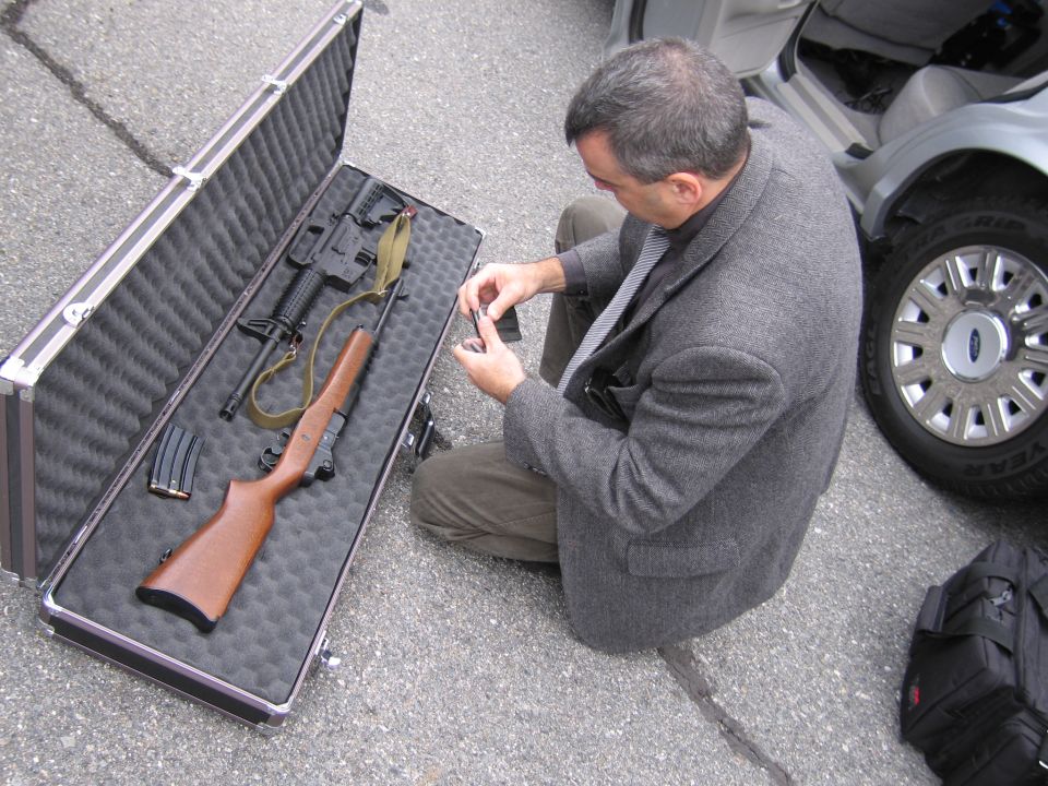 Man with guns in case next to silver car