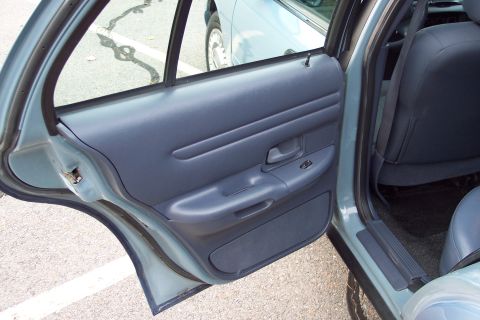 2001 Ford Crown Victoria - The interior door panel and rear seat of a car are shown, with another vehicle visible outside the window.