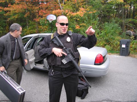 2001 Ford Crown Victoria - A police officer points while standing next to a silver sedan with a civilian holding a briefcase.
