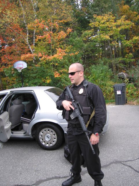 2001 Ford Crown Victoria - A police officer stands next to a silver sedan with the rear door open, during autumn.
