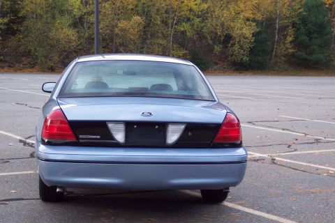 2001 Ford Crown Victoria - Rear view of a light blue 2001 Ford Crown Victoria parked in an outdoor lot with trees in the background.