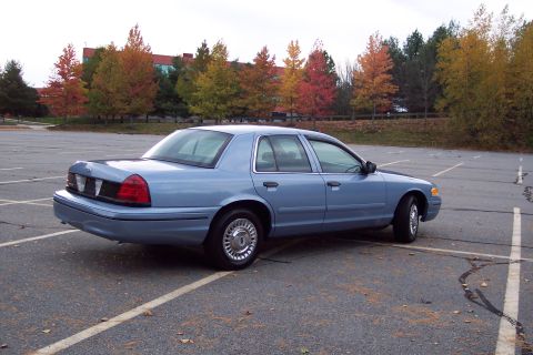 2001 Ford Crown Victoria - A blue 2001 Ford Crown Victoria is parked in an empty lot during autumn.