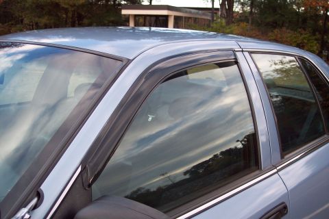 2001 Ford Crown Victoria - The side profile of a light blue sedan is shown, window rain guards and reflections in the glass.
