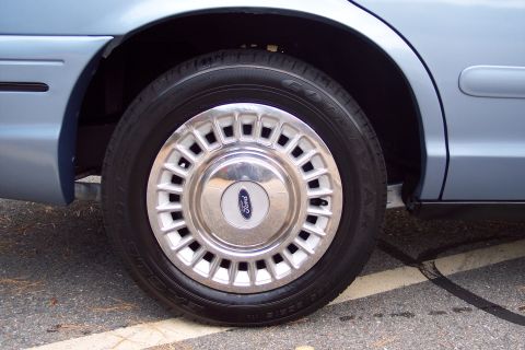 2001 Ford Crown Victoria - Close-up of a light blue car's wheel and fender, showing the Ford emblem on the hubcap.