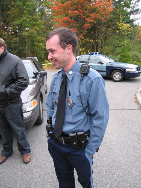 2001 Ford Crown Victoria - A police officer stands near a patrol car, with another police vehicle visible in the background during autumn.