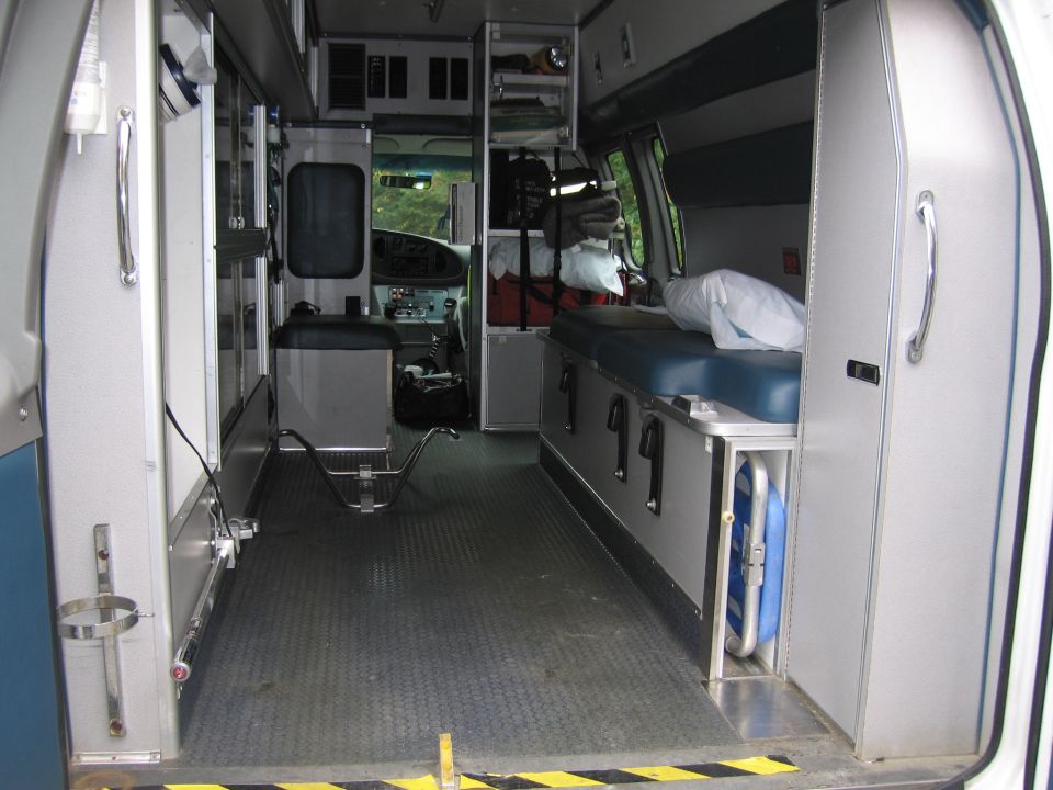 Ambulance interior showing patient bench, medical equipment storage, and driver's cabin view