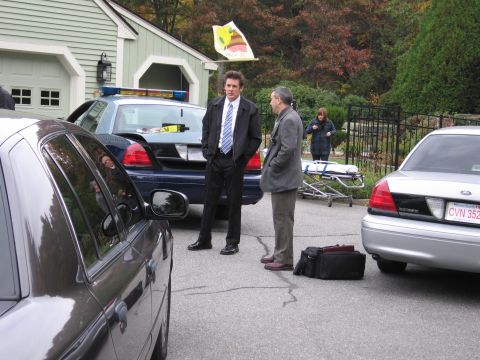 2001 Ford Crown Victoria - Two men in suits stand near a police car and another car parked in front of a house, with a stretcher nearby.