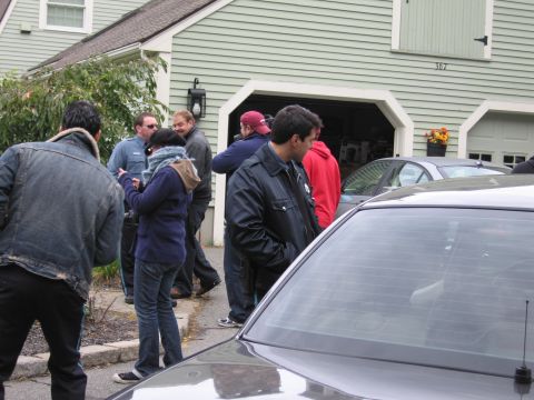 2001 Ford Crown Victoria - People are gathered outside a house with an open garage, with a dark sedan partially visible in the foreground.