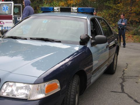 2001 Ford Crown Victoria - A police car is parked on the side of the road, with an ambulance and officers visible in the background.