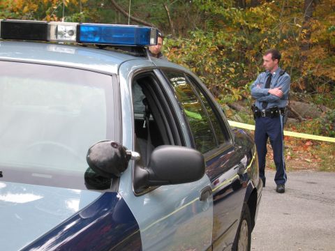 2001 Ford Crown Victoria - Police officer stands near a Ford Crown Victoria patrol car, with trees and yellow caution tape in the background.