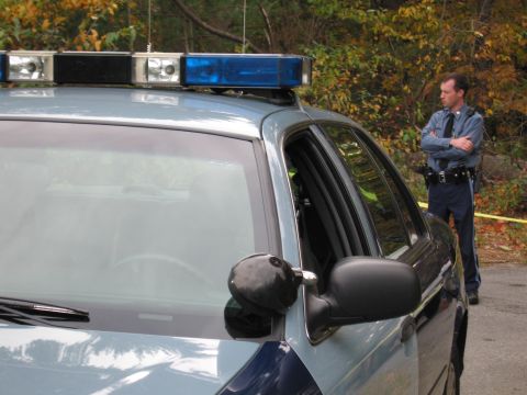 2001 Ford Crown Victoria - A police officer stands next to a patrol car, with trees in the background.