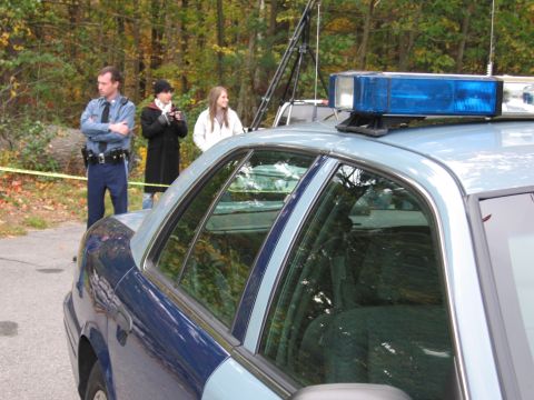 2001 Ford Crown Victoria - A police car is parked at a scene with officers and civilians present.