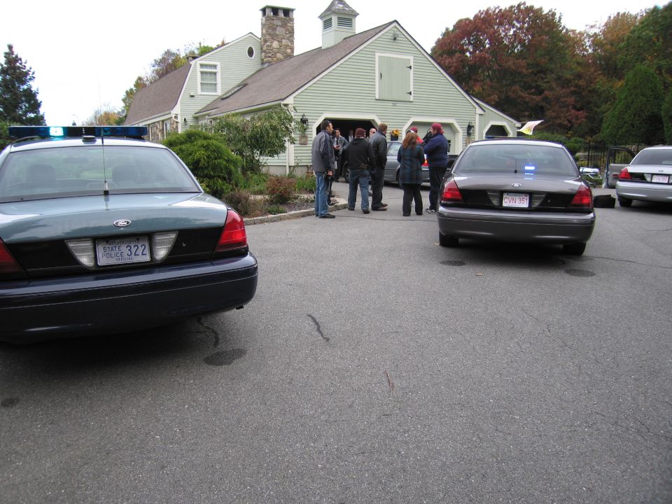 Rear view of two police cars, one dark green, one dark gray, parked in front of a house