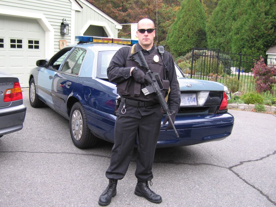 2001 Ford Crown Victoria police car, rear view, with officer holding rifle