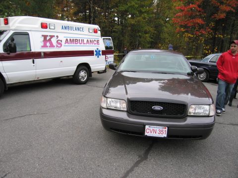 2001 Ford Crown Victoria - A gray 2001 Ford Crown Victoria is parked next to an ambulance, with a person in a red hoodie standing nearby.