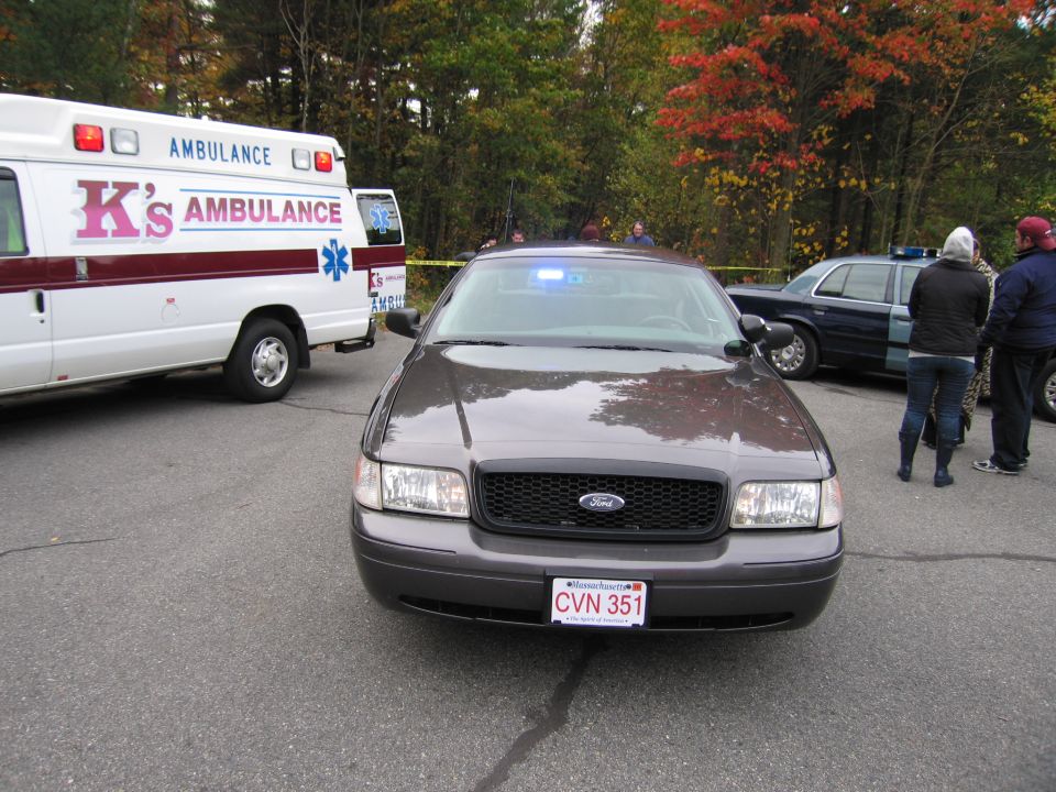 2001 Ford Crown Victoria police car with blue lights on, parked next to K's Ambulance van. Massachusetts license plate CVN 351