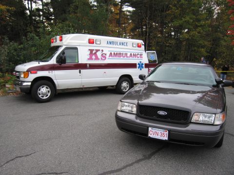 2001 Ford Crown Victoria - A Ford Crown Victoria and an ambulance are parked on an asphalt surface with trees in the background.