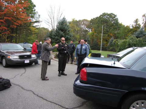 2001 Ford Crown Victoria - A dark blue Ford Crown Victoria is seen from the rear with its trunk open, while police officers stand nearby.