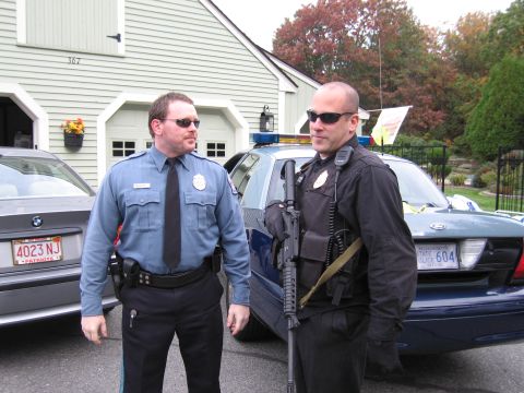 2001 Ford Crown Victoria - Two officers stand in front of a police vehicle and a civilian car outside a residential garage.