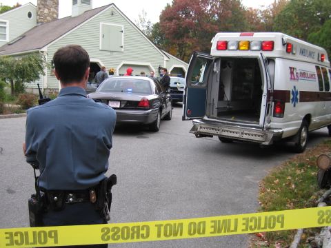 2001 Ford Crown Victoria - A police officer stands guard near a 2001 Ford Crown Victoria and an ambulance, with police tape cordoning off the scene.