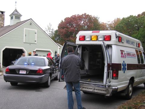 2001 Ford Crown Victoria - A police car and an ambulance are parked in front of a garage with people nearby.
