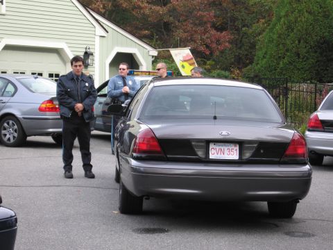 2001 Ford Crown Victoria - A 2001 Ford Crown Victoria police car is parked behind another vehicle, with officers standing nearby.