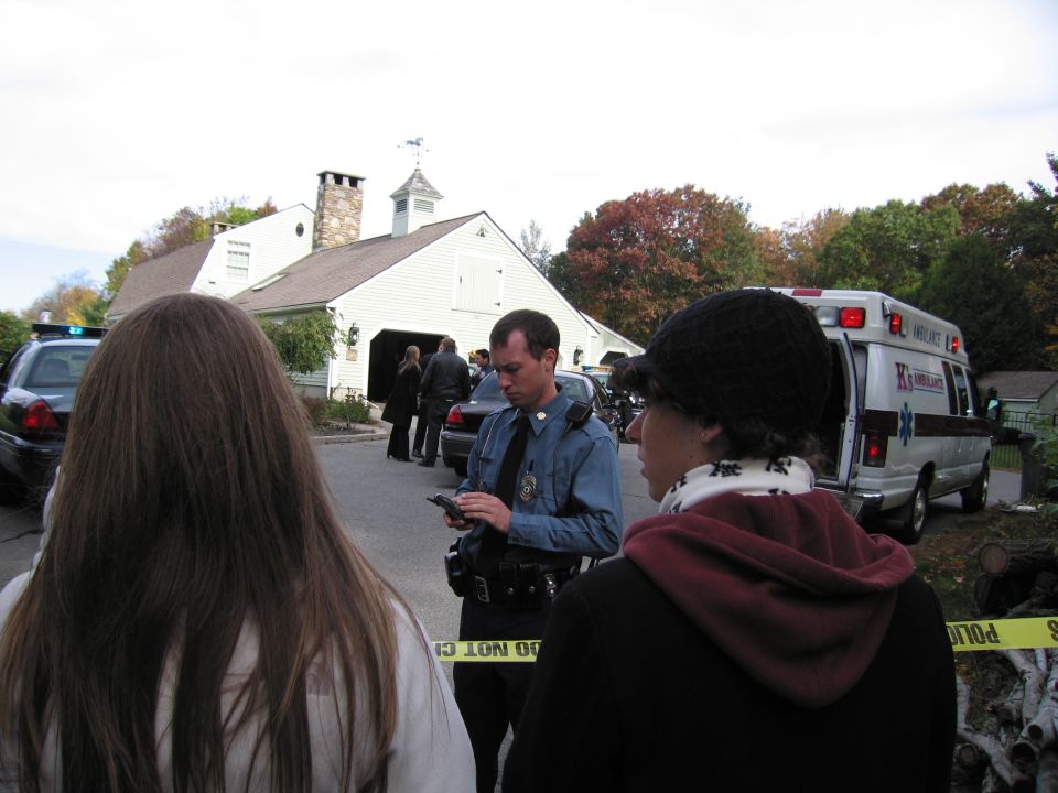 Police officer on phone with ambulance and police car behind yellow caution tape