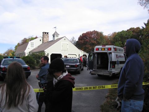 2001 Ford Crown Victoria - Police tape cordons off a scene involving a police car, an ambulance, and other vehicles outside a large house.