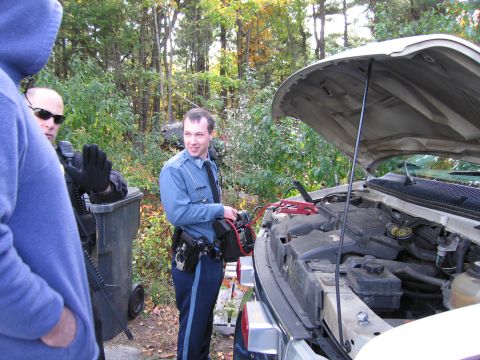 2001 Ford Crown Victoria - Two police officers are seen assisting with a vehicle, using jumper cables to start the engine of a van.