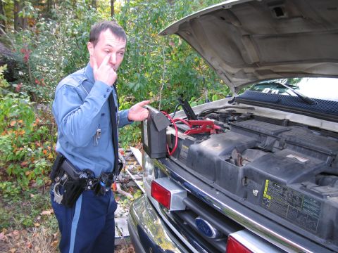 2001 Ford Crown Victoria - Officer attempts to jump-start a white Ford van with the hood open and jumper cables attached.