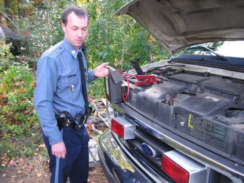 2001 Ford Crown Victoria - A police officer attempts to jump-start a white Ford E-Series van, which has its hood open and jumper cables connected.