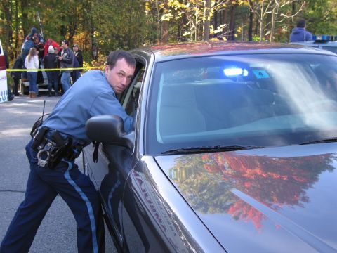 2001 Ford Crown Victoria - Officer leans into a 2001 Ford Crown Victoria, blue lights visible on the dash.