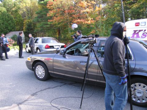 2001 Ford Crown Victoria - A dark gray Ford Crown Victoria is parked on a street, with a camera crew filming.