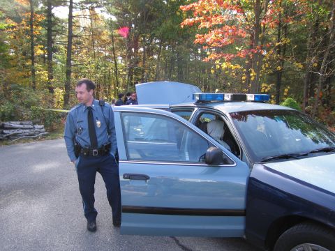2001 Ford Crown Victoria - A police officer stands next to a light blue police car with its driver's door open and emergency lights on the roof.